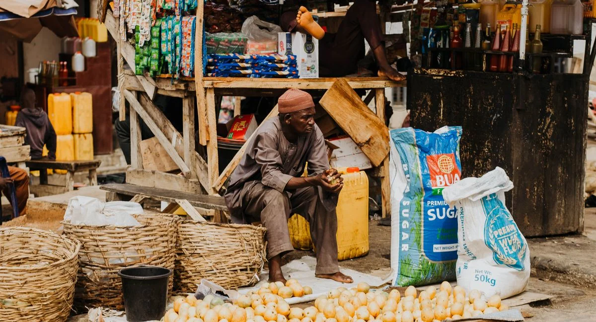 A street vendor in a bustling market selling produce and assorted goods in woven baskets.