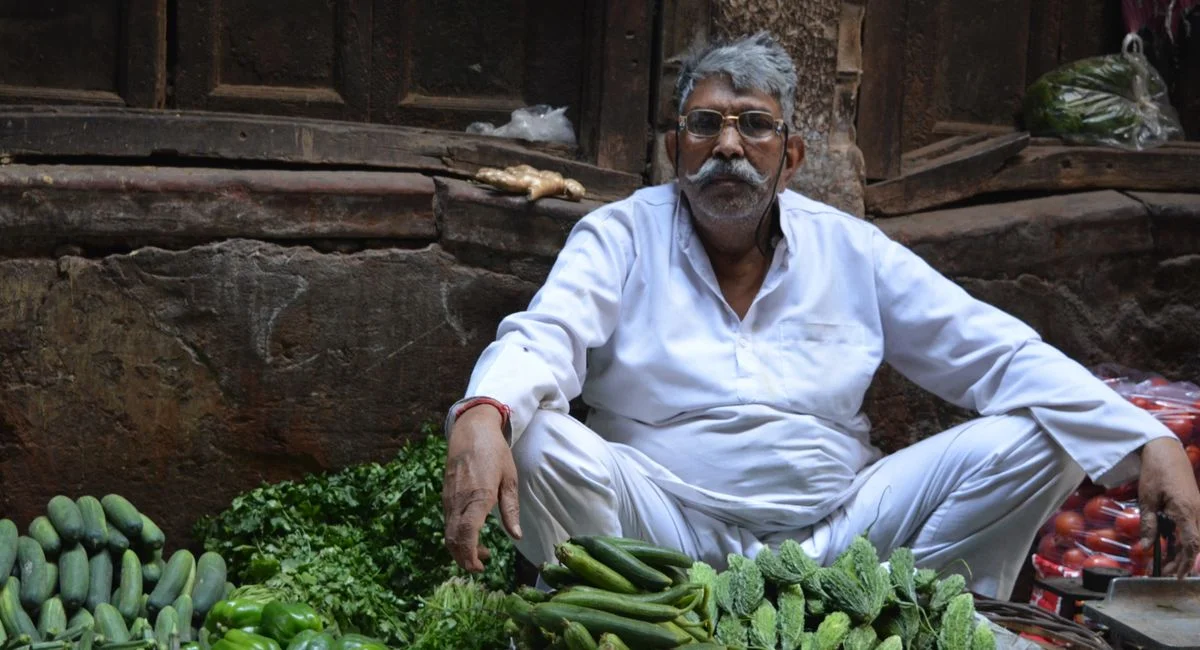 A local vegetable seller sits amongst fresh produce in Old Delhi market, India.