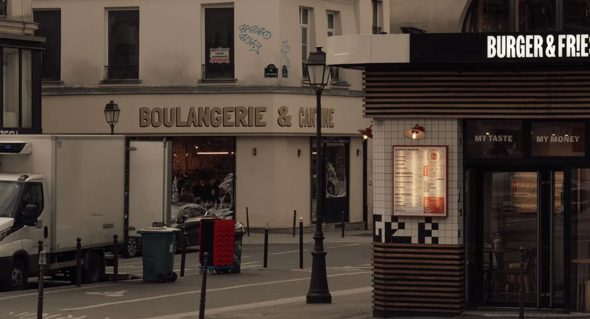 Evening view of a Paris street corner featuring a boulangerie and a burger shop, capturing city life and French architecture.