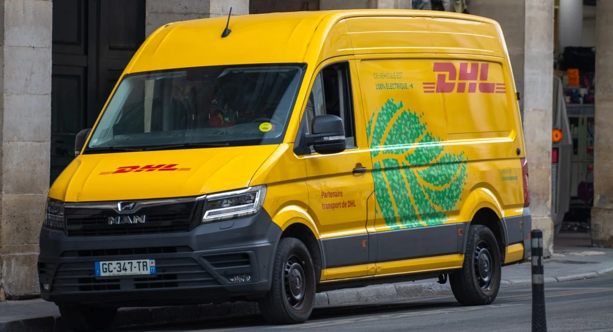 A yellow DHL electric delivery van parked on a street in Paris, France.