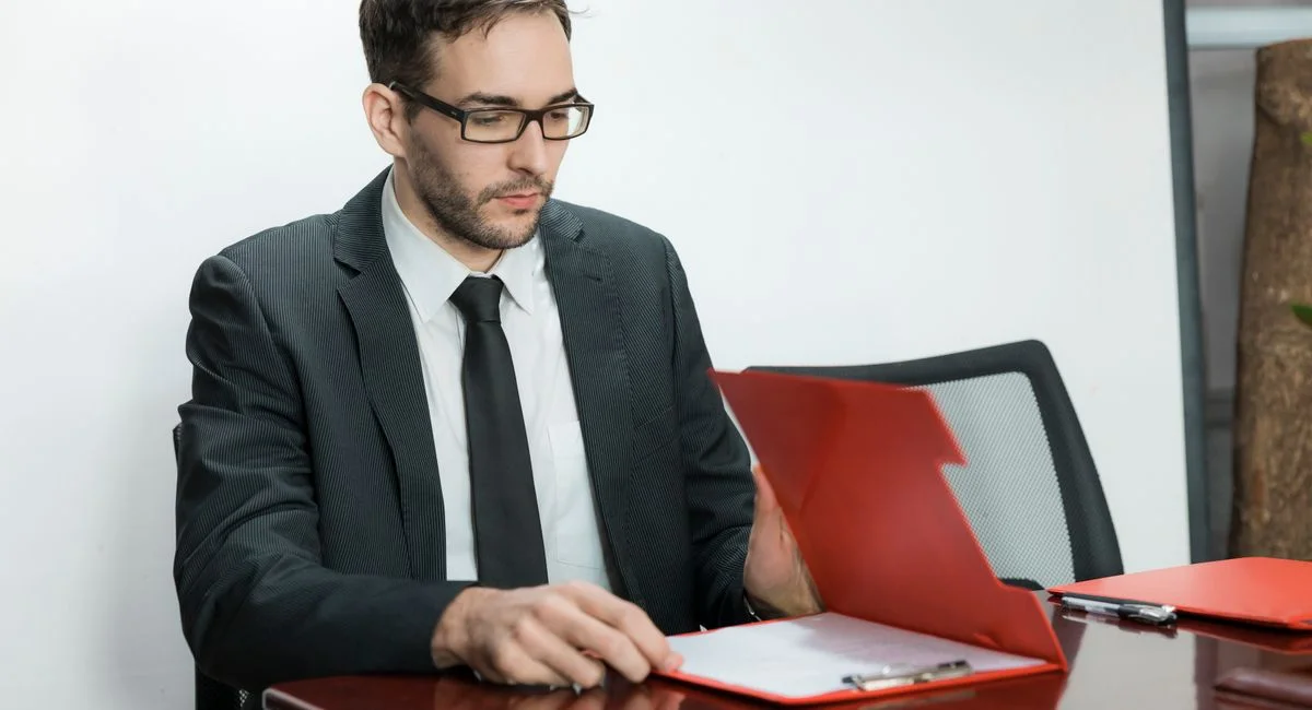 Professional man in suit reviewing papers at office desk with focus and determination.