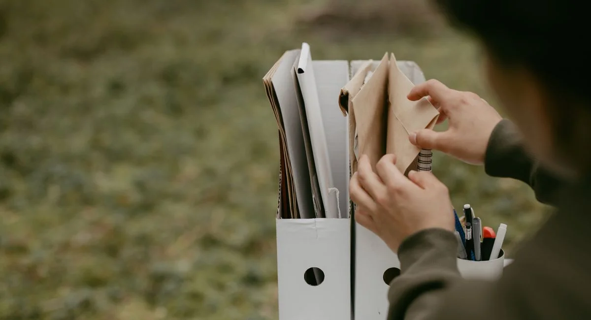 Person sorting documents in folders outdoors, hands visible, neutral tone.