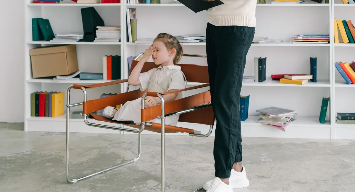 A child in a therapy session with a therapist holding a clipboard.