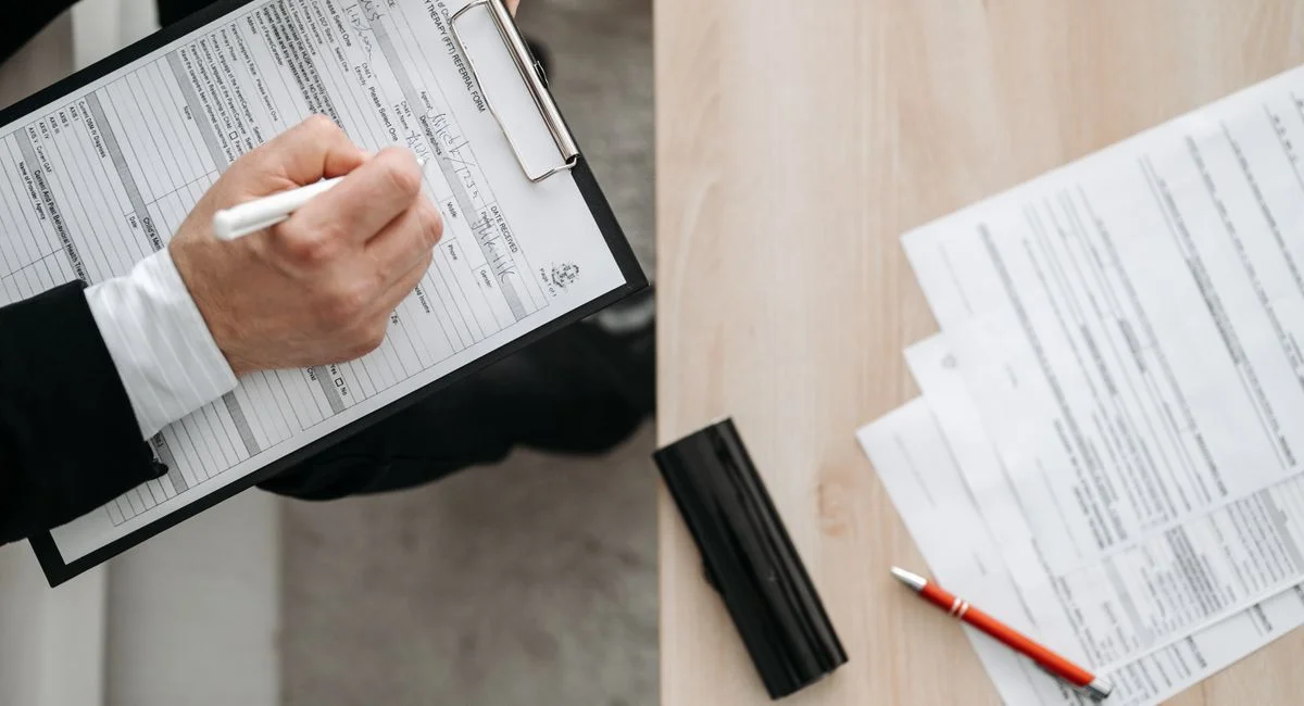 High-angle view of a person filling out forms on a clipboard, emphasizing paperwork and documentation.