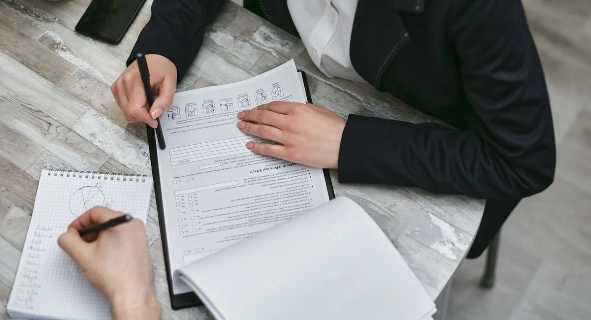 Two colleagues reviewing documents and taking notes during a business meeting.
