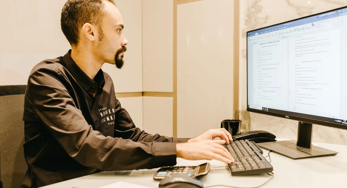 Young man focused on typing, working on computer in sleek, modern office.