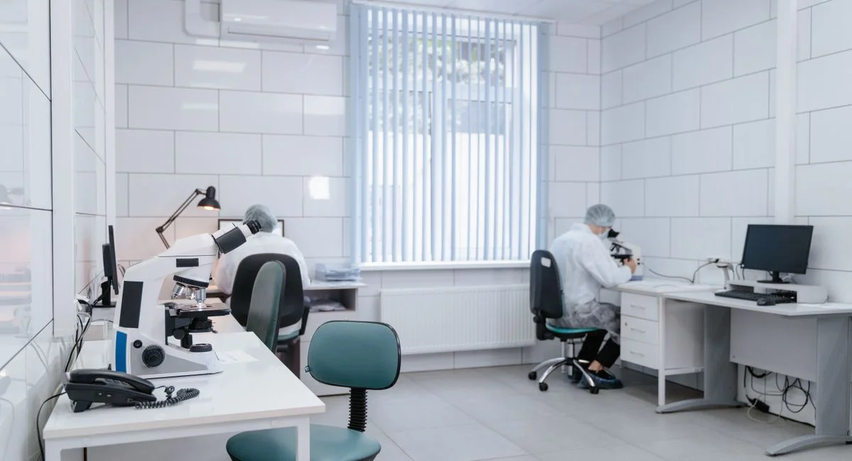 Clean, modern laboratory interior with microscopes and researchers in protective gear conducting analysis.