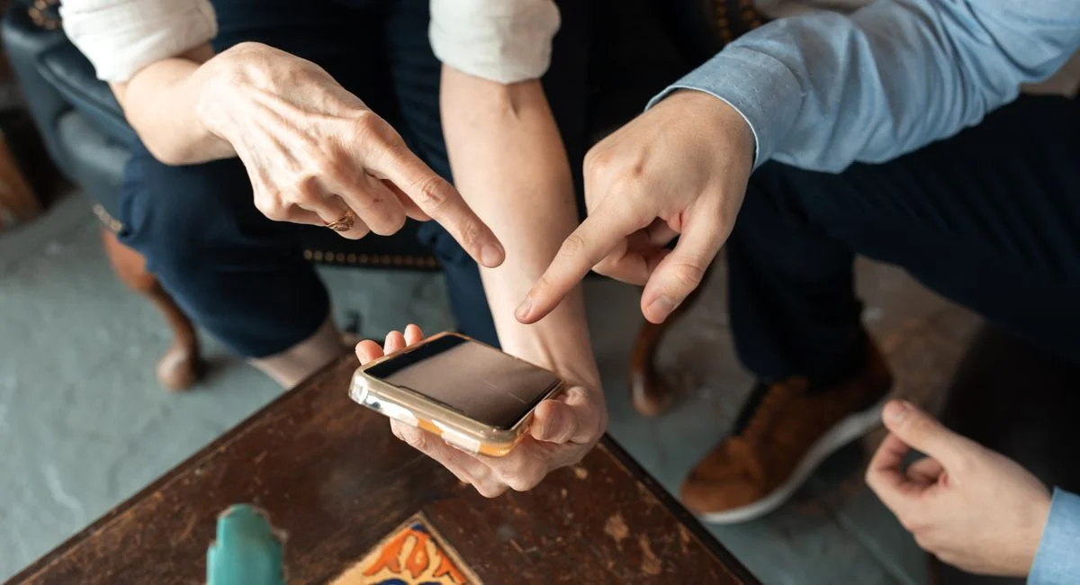 Two people engaged in discussion, pointing at a smartphone on a table indoors.