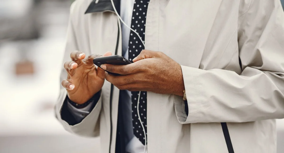 Close-up of a businessman using a smartphone and headphones outdoors.