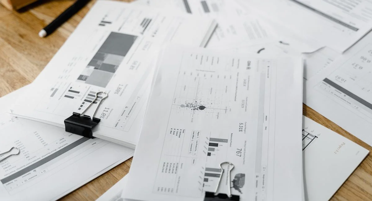 A stack of financial reports and graphs with clips on a wooden desk, highlighting business planning.