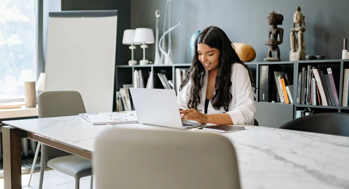 Woman using laptop at a stylish office desk, working on projects in a modern environment.