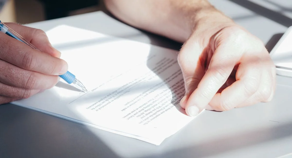 Hands signing a contract with a blue pen, close-up view.