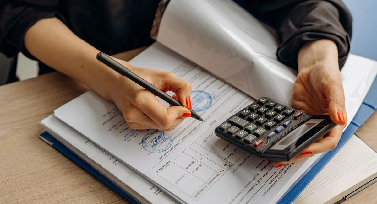 An accountant using a calculator and signing paperwork, showcasing financial analysis.