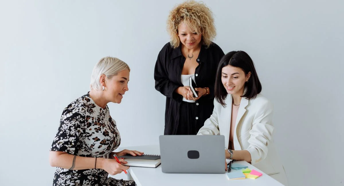 Three diverse women engaged in a productive business meeting in a minimalist office space.