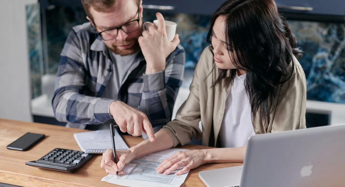 A couple analyzing financial documents with calculator and laptop on a table.