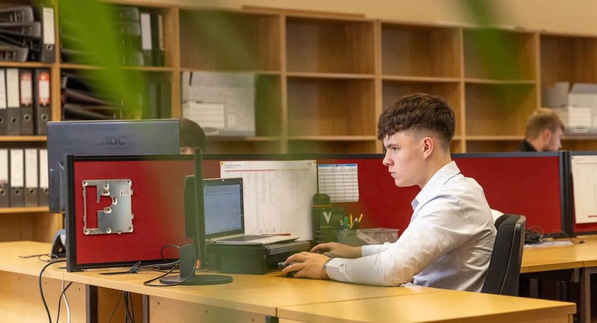 A focused young man typing on a computer in a contemporary office environment.