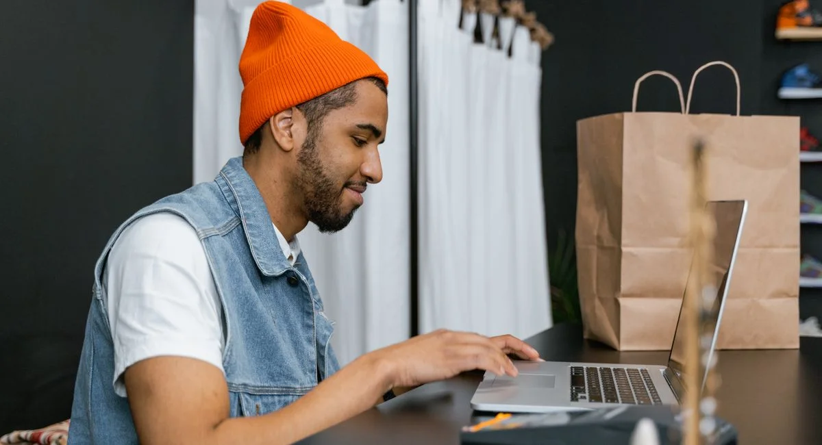 Man in a beanie using laptop in a stylish fashion store, indoors.