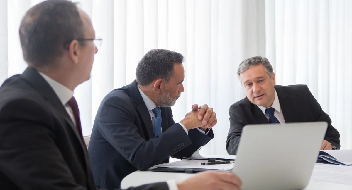 Three businessmen collaborating during a meeting around a laptop in a bright office.