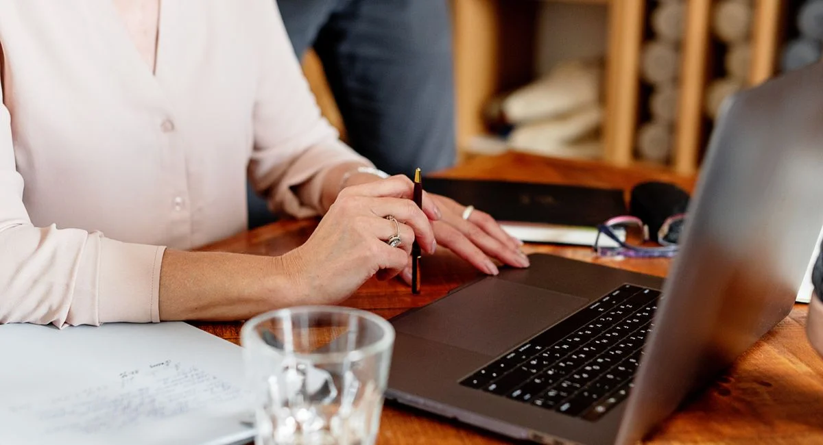Close-up of a woman working on a laptop with documents on a desk. Ideal for business themes.