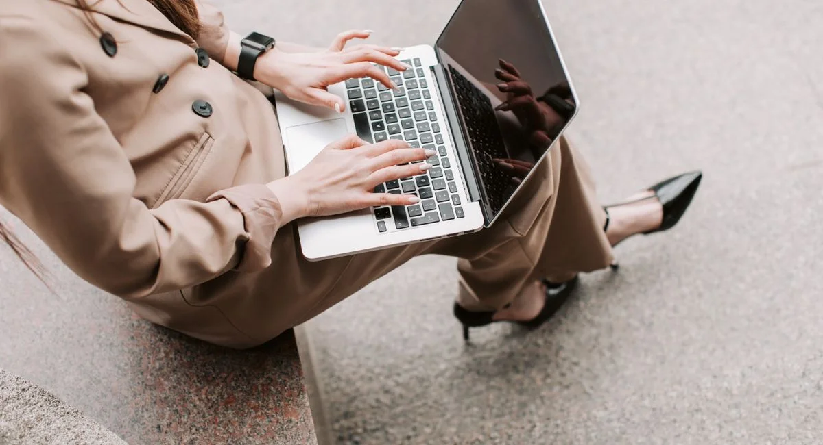 Professional woman in corporate attire typing on a laptop outdoors