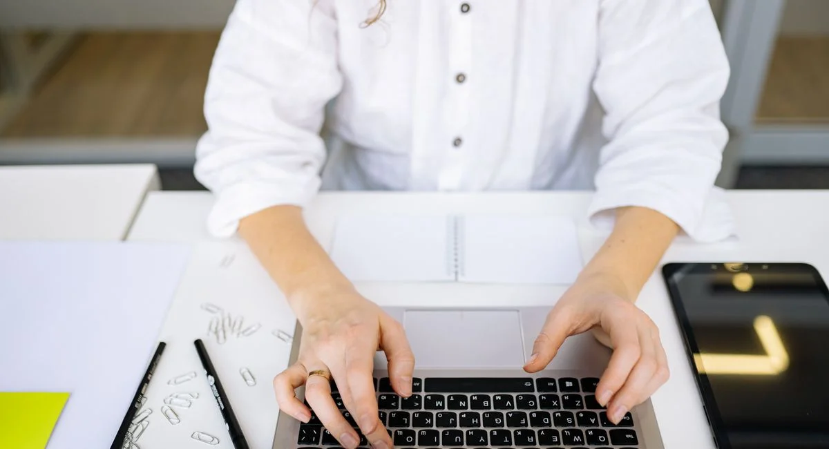 Close-up of woman's hands typing on laptop keyboard in bright, modern office space. Ideal for work and technology themes.