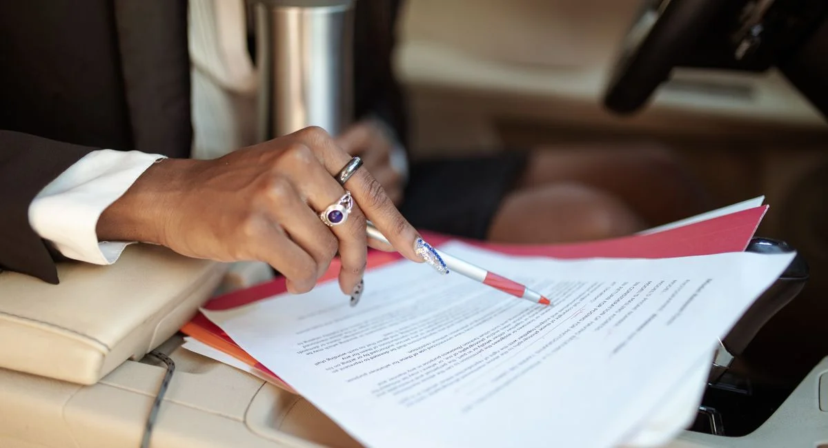 A professional reviewing documents in a car interior, focusing on hand and paperwork.