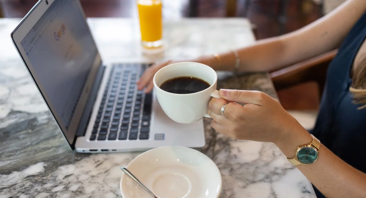 A woman in a café working on a laptop, holding a cup of black coffee, creating a productive atmosphere.
