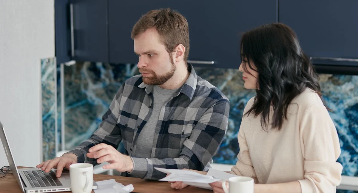 A couple working together on a laptop managing finances at home, showcasing teamwork and concentration.