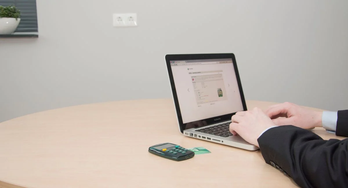 A professional working on a laptop at a round table with a card reader nearby.