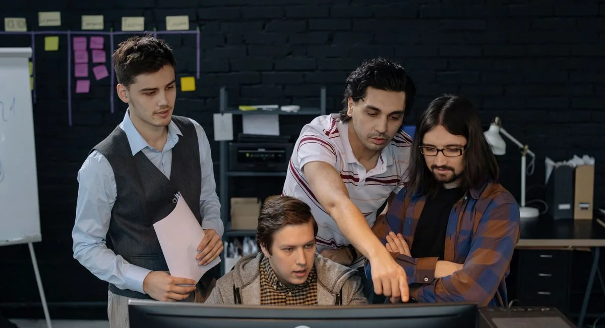 Group of professionals discussing a project at a computer in a modern office environment.