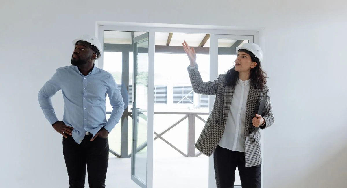 Two contractors inspecting a modern house interior wearing hard hats.