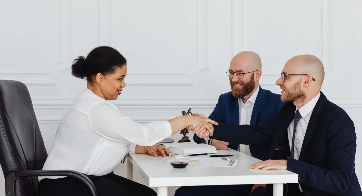 Business meeting with diverse professionals in office attire shaking hands.