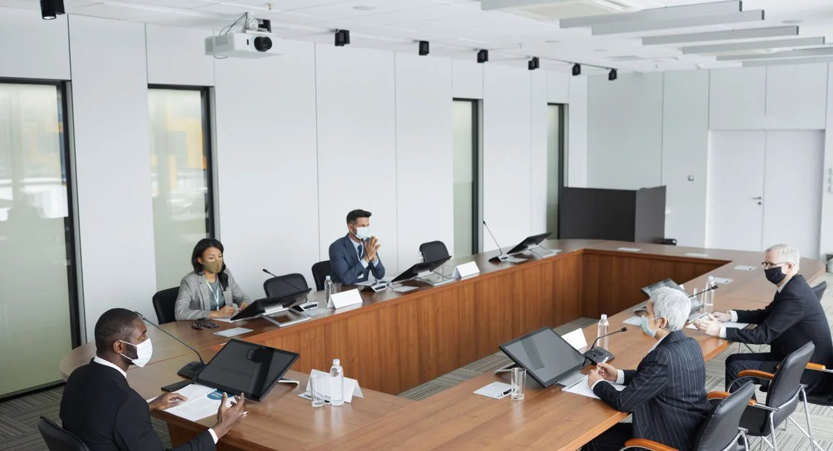Business professionals wearing masks attending a conference meeting in a modern setting.