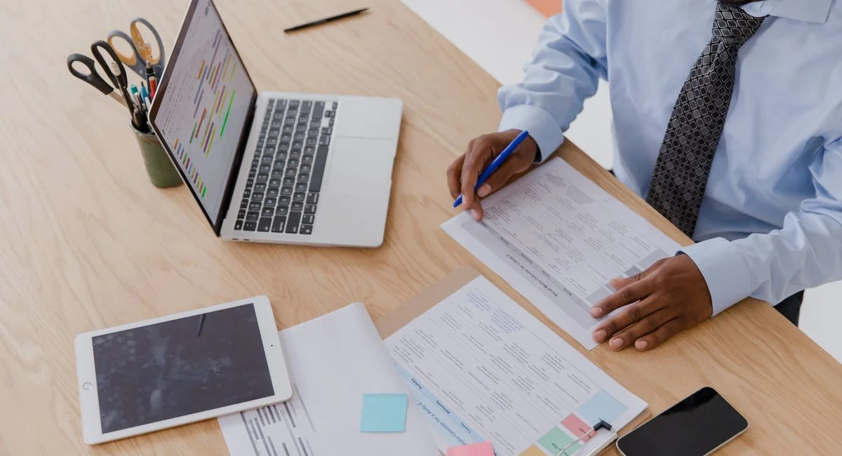 High angle view of a businessman working at a desk with a laptop, tablet, and documents.
